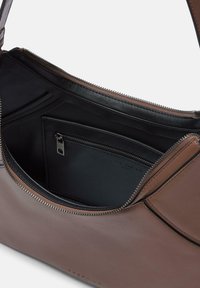 Borsa a tracolla in pelle marrone con chiusura a zip, dotata di un interno nero, organizzazione con più tasche e dettagli di cucitura sottili.