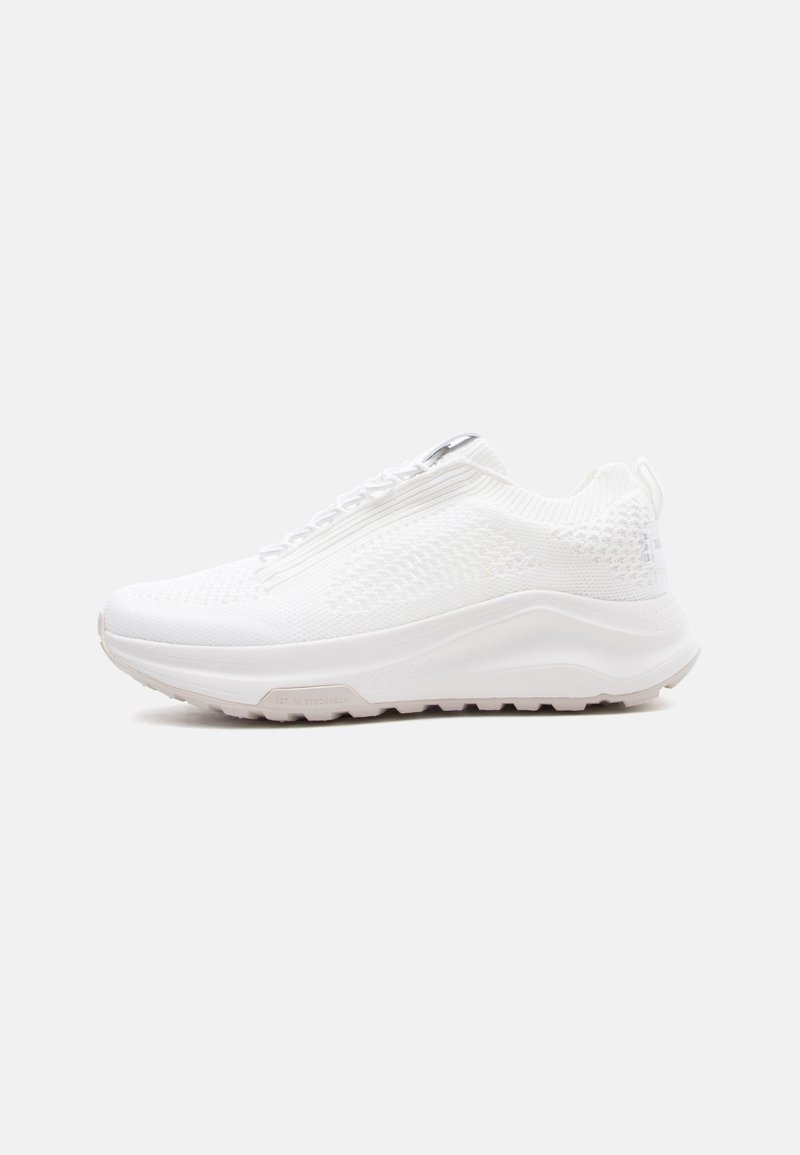White knitted athletic sneaker with thick sole and textured grip, side view on plain gray background.