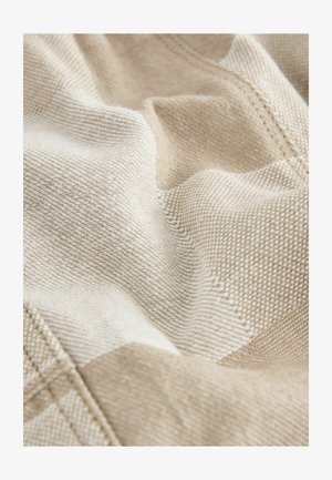 Bež i krem teksturirani materijal s tkanim uzorkom, koji sadrži dijagonalne pruge i vidljive šavove. Mekan, padajući izgled.