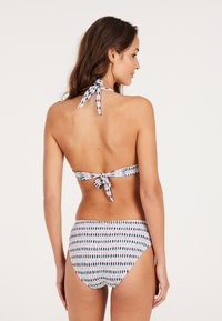 Bikini set koji uključuje gornji deo s vezanjem oko vrata i visoke gaćice s uzorkom, s geometrijskim oblicima u plavoj, crvenoj i beloj boji na svetloj pozadini.