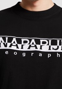 Black cotton t-shirt with a round neckline featuring a large embroidered white logo and text in a bold, stylized font across the chest.