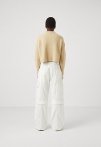 Maglione corto beige a coste abbinato a pantaloni cargo bianchi oversize con grandi tasche laterali e vita a contrasto.