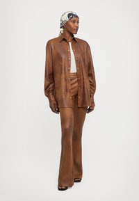 Brown leather shirt and pant set with a shiny finish, featuring a button-up design and long sleeves. Accessories include a patterned headscarf.