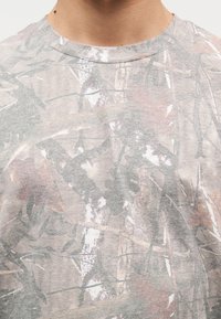 Γκρι μπλουζάκι με σχέδιο παραλλαγής σε απαλά γήινα χρώματα, με στ ρογγυλή λαιμόκοψη και κοντά μανίκια, κατασκευασμένο από απαλό, ελαφρύ ύφασμα.