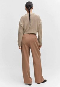 Beiger, gestrickter, kurz geschnittener Pullover mit geflochtenen Details und braune, weit geschnittene Hose. Glatte Textur, schlichtes Design und maßgeschneiderte Passform.