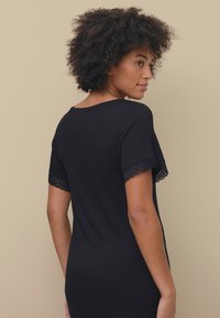 Sort kjole med korte ærmer med blondedetaljer, rund halsudskæring og tætsiddende design. Glat tekstur med en diskret glans.