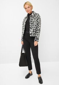 Jasje van faux bont met luipaardprint, zwarte coltrui, op maat gemaakte zwarte broek, elegante zwarte loafers en zwarte handtas op een witte achtergrond.
