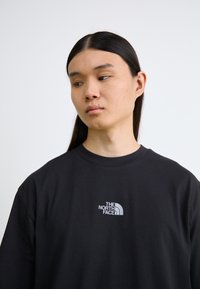 Svart bomullst-skjorte med korte ermer og rund hals, med en liten grå logo av "The North Face" på venstre brystområde.