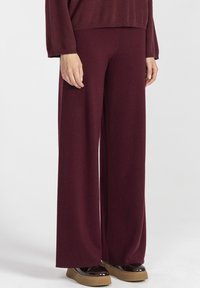 Kobieta w luźnych bordowych dzianinowych spodniach i dopasowanej bluzie, w połączeniu z ciemnobrązowymi butami na platformie z jasnymi podeszwami.