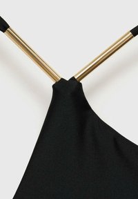Crni materijal s teksturiranom površinom, obješeno pod trokutastim kutom, pričvršćeno za dva zlatna metalna štapa, čineći elegantan dizajn.