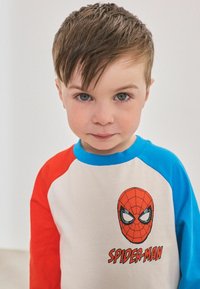 Rode en blauwe lange mouwen t-shirt met een Spider-Man graphic op een crèmekleurige basis, met een ronde halslijn en een zachte stoftextuur.