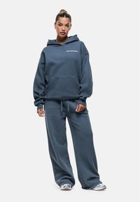 Felpa blu oversize e pantaloni abbinati in tessuto morbido. Presenta una tasca frontale e un logo del marchio discreto sul petto.