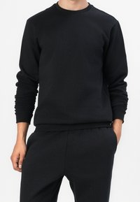 Felpa nera in misto cotone, con scollatura rotonda e polsini a costine. Il design è semplice, senza motivi o decorazioni prominenti.