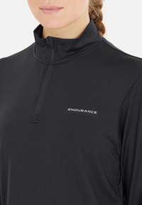Musta pitkähihaisa paita, jossa on puolivetoketjullinen kaulus ja sana "ENDURANCE" valkoisella, valmistettu sileästä ja venyvästä kankaasta.