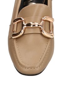 Mocasines de cuero beige con una hebilla dorada brillante y detalles de costura a lo largo del borde. Suela plana con ligero redondeo en la punta.