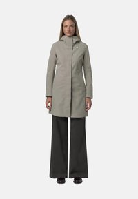 Cappotto impermeabile grigio chiaro con colletto alto e chiusura a zip. Abbinato a pantaloni larghi scuri. Presenta un design minimalista e un accento con logo.