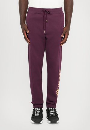 Lilla fleece joggebukser med snor i livet, slim fit og logo i gulltone. Kombinert med svarte joggesko med hvit skrift.