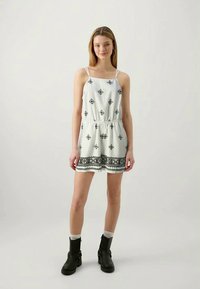 White sleeveless dress with black geometric patterns and trim. Elastic waistband, above-knee length, paired with black ankle boots.