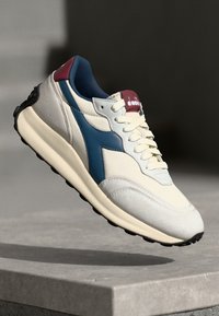 Cream and blue sneaker with a textured suede and mesh upper, white midsole, and black outsole. Features a maroon accent on the heel.