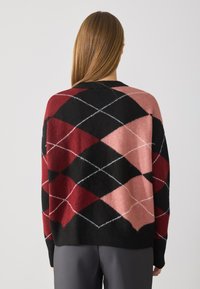 Pull en tricot avec un motif argyle dans des nuances de rouge, rose et noir, avec des accents blancs, une coupe décontractée et un col ras du cou.