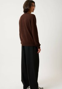 Pull en laine brun avec des poignets côtelés, associé à un pantalon large noir. Le pull a un col rond et une coupe décontractée.