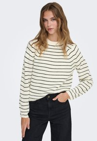 Pull crème à rayures horizontales noires, texture tricotée, col rond et manches longues. Associé à un jean noir.