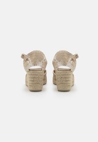 Beige kile høye sandaler med en strukturert vevd overdel og justerbar ankelstropp, med en jute-wrapped hæl for økt høyde og komfort.