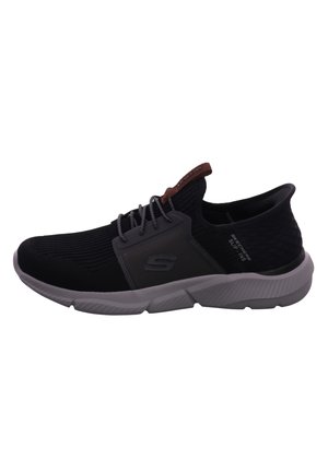 Zapatilla deportiva negra con parte superior de malla, acentos grises y una suela acolchada. Presenta una etiqueta marrón en el talón y detalles texturizados en el costado.
