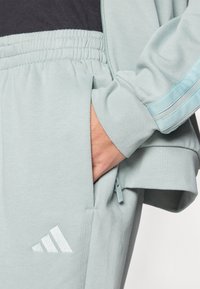 Világoskék sportdzseki cipzáras zsebbel és elasztikus mandzsettákkal. Hímzett logóval és sima szövettextúrával rendelkezik.