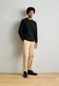 Black knitted sweater, beige cargo pants with side pockets, and black shoes. The fabric has smooth texture and relaxed fit. Simple design.