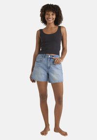 Jasnoniebieskie szorty dżinsowe z pięcioma kieszeniami i postrzępionym wykończeniem, zestawione z czarnym prążkowanym topem na ramiączkach, prezentowane na modelce.