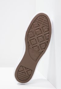 Bílé tenisky s texturovanou hnědou gumovou podrážkou se geometrickým vzorem. Obsahují branding "Converse All Star."