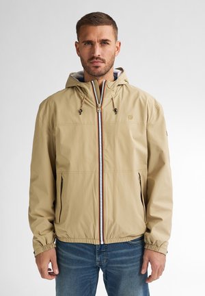 Beige gewatteerde jas met elastische manchetten, ritssluiting aan de voorkant en contrasterende details. Beschikt over twee zijzakken en een lichtgewicht materiaal.