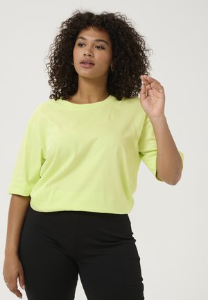 Neon žluté oversized tričko s krátkým rukávem, kulatým výstřihem a měkkou texturou. V kombinaci s černými klasickými kalhotami, které mají volný střih.