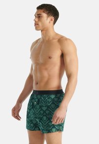 Boxerky z zelené látky se vzorem květin, černý elastický pas s knoflíkovým detailem a volný střih.