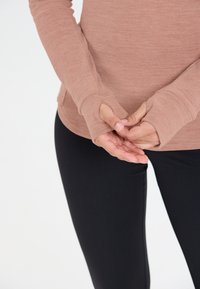 Langärmliges, sanft rosenfarbenes Oberteil mit Daumenlöchern, kombiniert mit schwarzen Leggings. Verfügt über eine weiche Textur und eine enganliegende Passform.