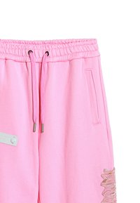 Pantalones de chándal rosas con cintura elástica, cordones, bolsillos laterales y un detalle texturizado con volantes a lo largo de un lado.