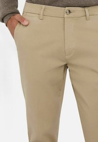 Chinos beige con una textura suave, que cuentan con bolsillos delanteros y un cierre de botón metálico. Diseño clásico de pierna recta, con detalles de costura simples.
