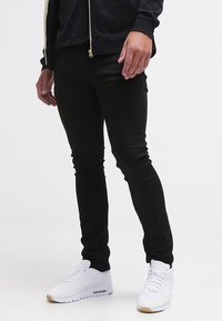 Pantalones negros de corte ajustado, hechos de una tela elástica, con una textura suave y un diseño minimalista. Combinados con zapatillas deportivas blancas.
