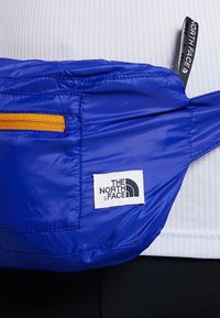 Blå nylon midjeväska med en orange dragkedja, med en vit logotypetikett från "The North Face." Slät, lätt material, kompakt design.