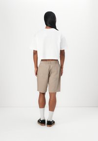 Vit kortärmad t-shirt, beige shorts med elastisk midja, medellång. Svarta skor med gummisålar, vita strumpor. Minimalistisk design; inga mönster.