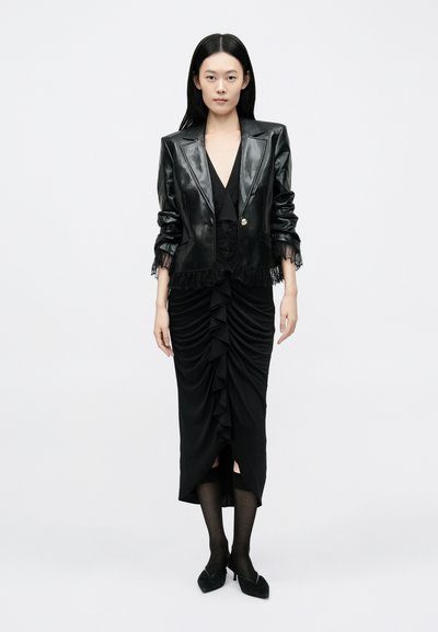 Fekete bőrkabát szakadt csipke díszítéssel, hozzáillő fekete, csavart fodrokkal díszített testhezálló ruha. Fekete áttetsző harisnya és hegyes orrú lapos cipő.