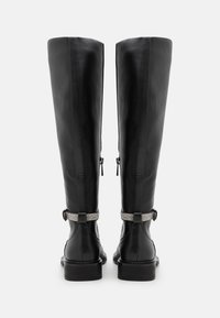 Bottes en cuir noir montant jusqu'au genou avec une texture lisse, ornées d'un accent décoratif en strass sur la boucle et une semelle épaisse.