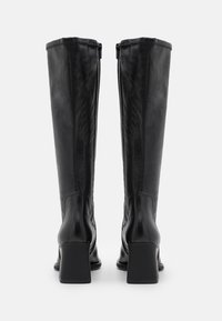 Botas de cuero negras hasta la rodilla con un tacón cuadrado, textura suave y cremalleras laterales visibles; diseño elegante y caña ajustada.