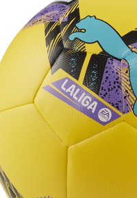 Geltona futbolo kamuolys su tekstūruota paviršiumi, dekoruotas purpurinėmis ir juodomis akcentais, LaLiga logotipu ir EA Sports prekės ženklu.