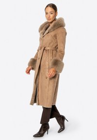 Beżowy płaszcz z zamszu z kapturem i mankietami wykończonymi futrem, z paskiem w talii i bocznymi kieszeniami; prosty krój, miękka faktura i średnia długość.