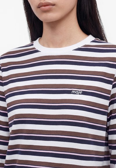 Γυναίκα που φοράει μακρυμάνικο πουκάμισο με οριζόντιες καφέ, ναυτικές, ροζ και λευκές ρίγες και μικρό λογότυπο «maje» στο στήθος.