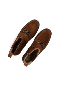 Bruine suède schoenen met een gladde textuur, ronde vorm, decoratieve metalen accenten en een lipje aan de achterkant voor gemakkelijk aan- en uittrekken.