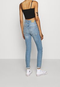 Jeans de denim azul claro de cintura alta, con un ajuste slim, puños enrollados y bolsillos traseros, combinados con zapatillas altas blancas.