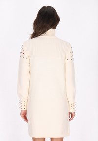 Cremefarvet turtleneck sweater kjole med ribbet tekstur, dekoreret med farverige nitter på ærmerne og en afslappet pasform.